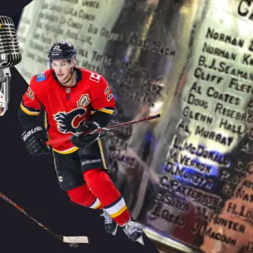 Hockey player in red jersey skating on ice near a Stanley Cup trophy.