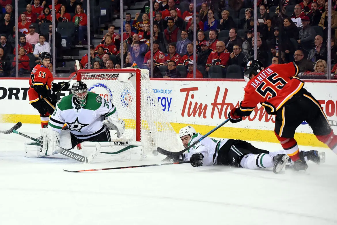 Hockey player scores a goal past the goalie and defender.