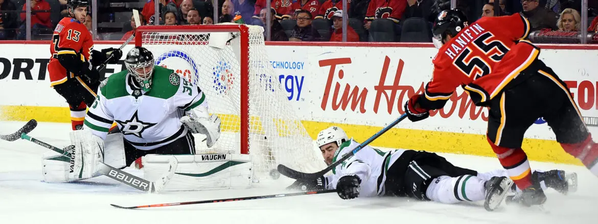 A hockey player in white slides on the ice near the opposing goal during a game.