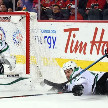 A hockey player in white slides on the ice near the opposing goal during a game.