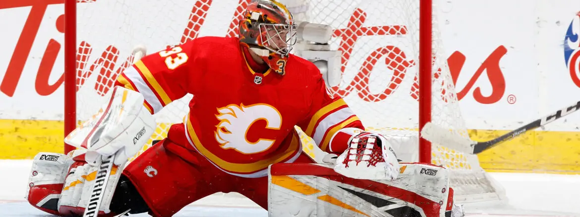 Hockey goalie in red Calgary Flames uniform making a save.