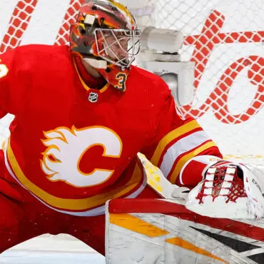 Hockey goalie in red Calgary Flames uniform making a save.
