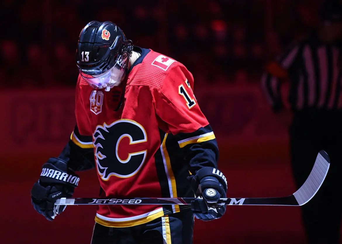 Hockey player in red Calgary Flames jersey holding a stick on ice.