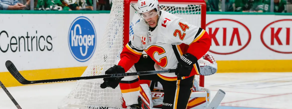 Hockey player in white Calgary Flames jersey handling puck near goal.