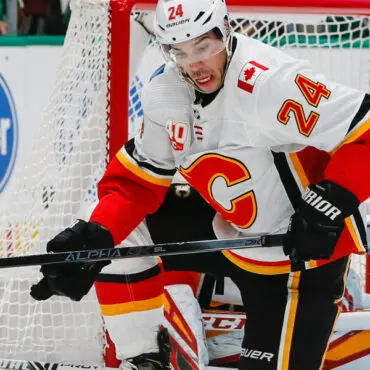 Hockey player in white Calgary Flames jersey handling puck near goal.