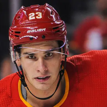 Close-up of a focused hockey player in a red helmet and jersey.