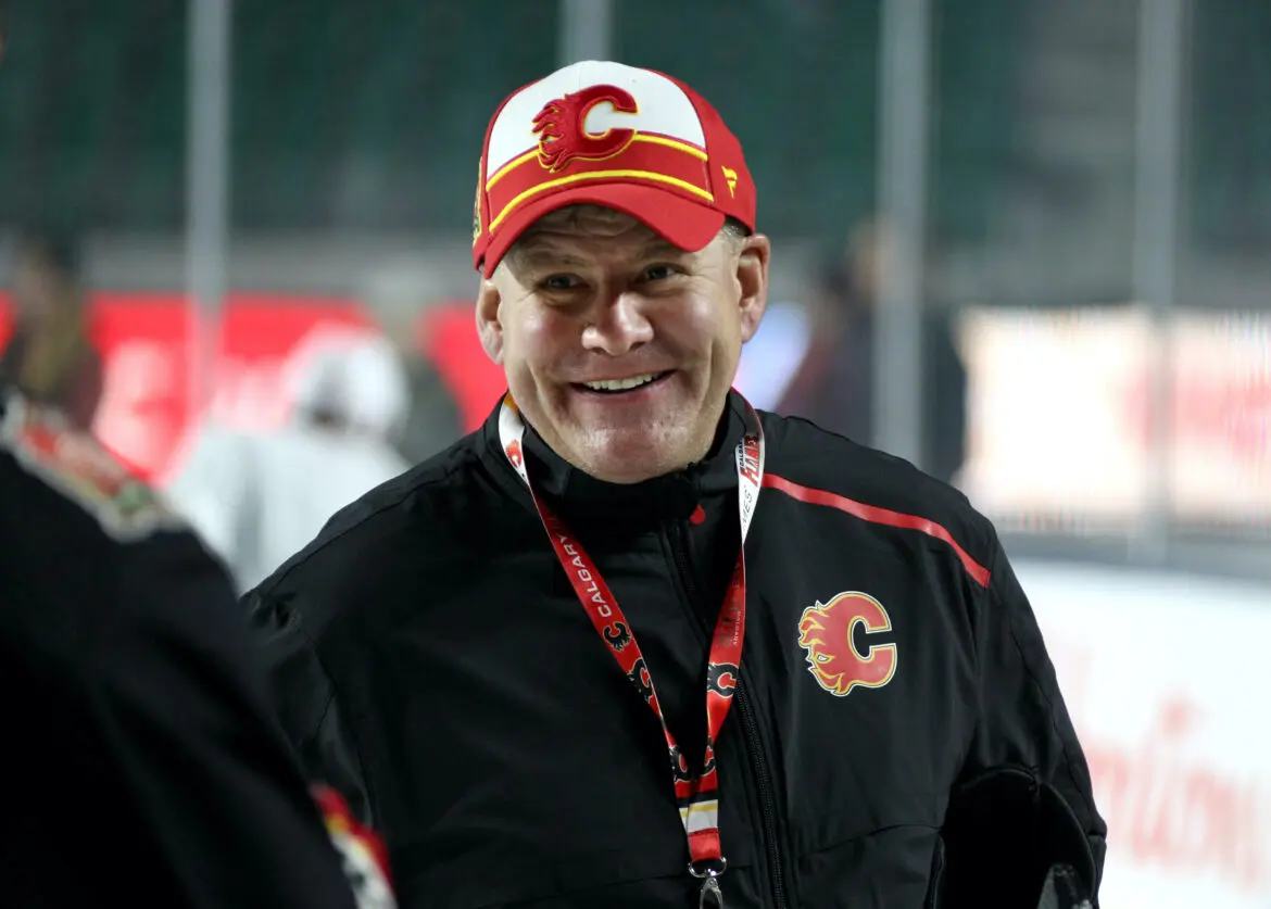 A man wearing Calgary Flames gear smiles outdoors.