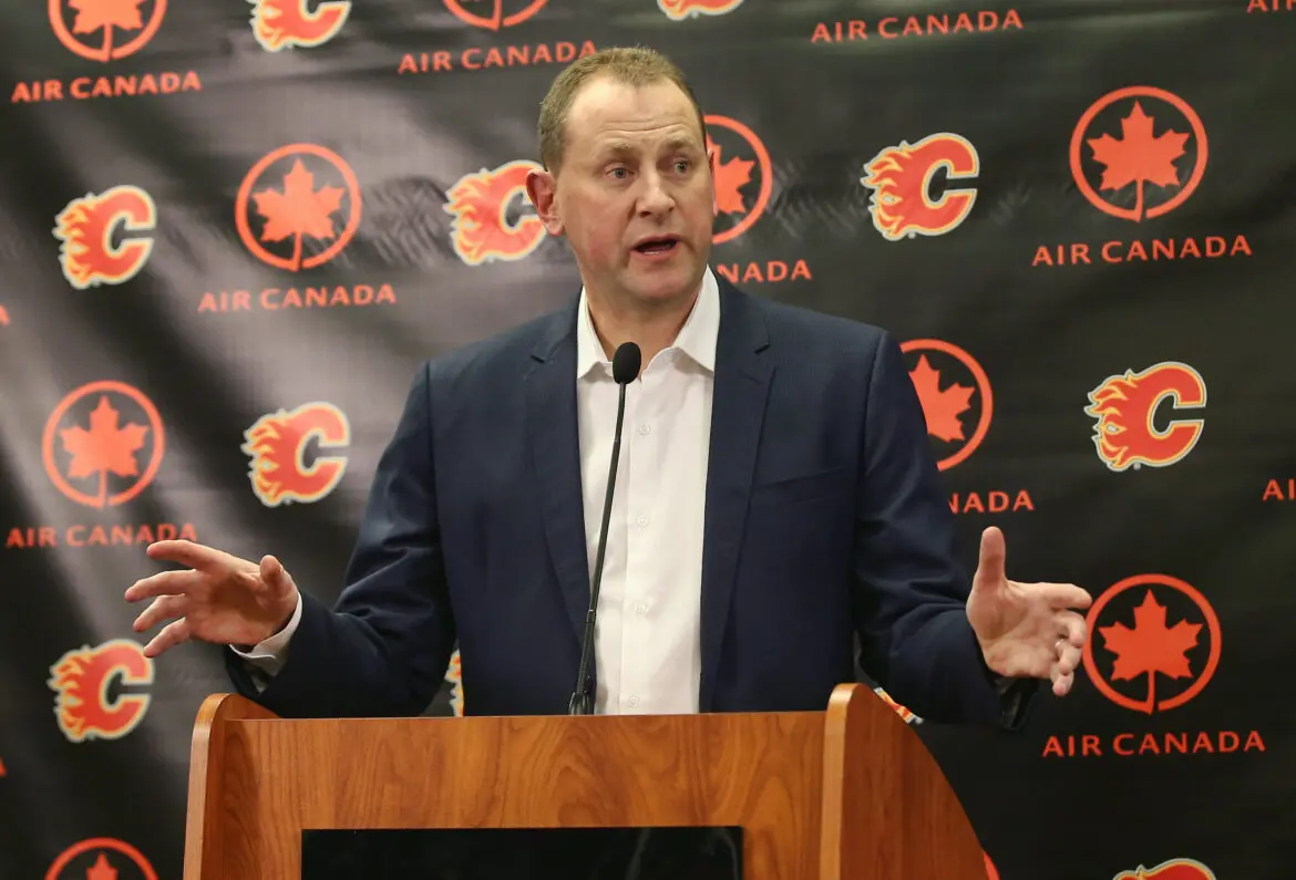 Man speaking at a podium with Calgary Flames logos in the background.