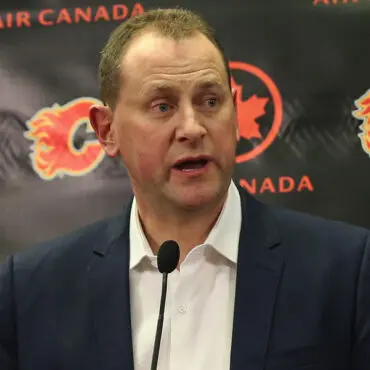 A man speaking at a press conference with sports logos in the background.