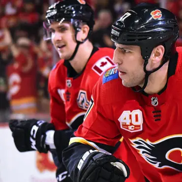 Two hockey players in red jerseys on the bench during a game.