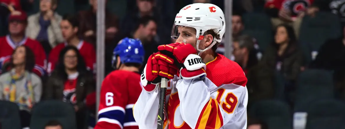 Hockey player in red jersey covering his mouth with gloved hands on the ice.