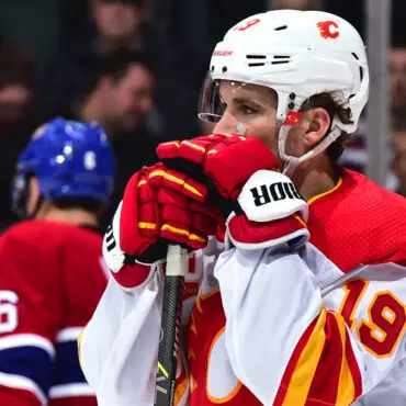 Hockey player in red jersey covering his mouth with gloved hands on the ice.