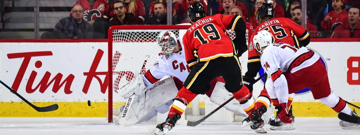 Hockey player in red jersey preparing to score against goalie in white gear.
