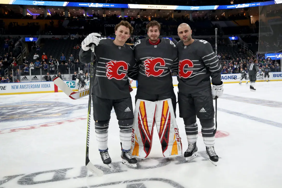 Three hockey players in Calgary Flames gear pose on ice rink.