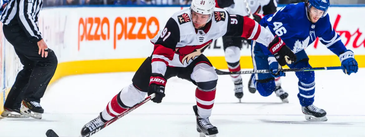 Ice hockey player in white and black uniform skating on ice during a game.