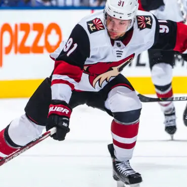 Ice hockey player in white and black uniform skating on ice during a game.