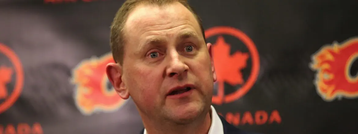 A man speaking with a serious expression in front of a black and red background.
