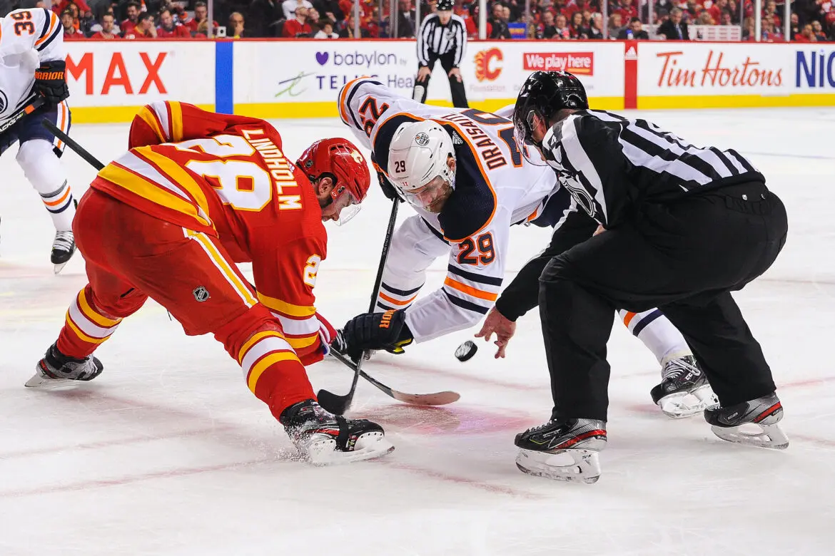 Two ice hockey players face off at the start of a play with a referee dropping the puck.