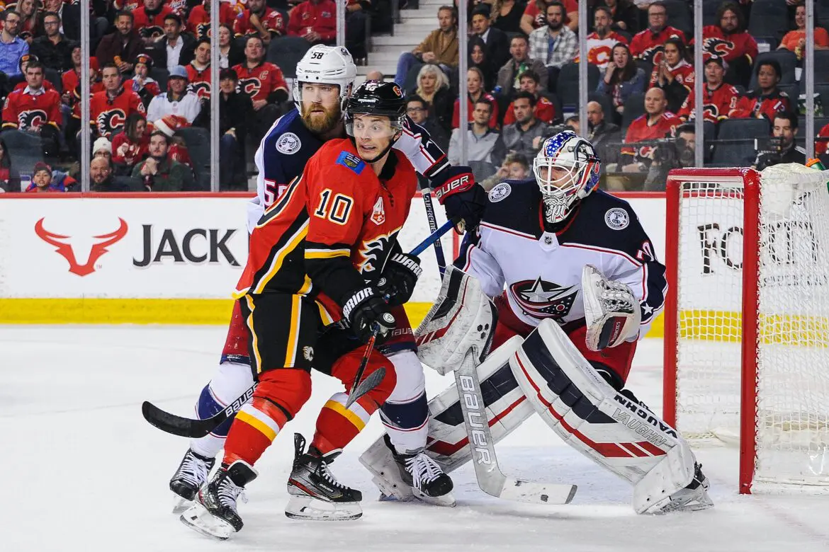 Hockey players from Calgary Flames and Columbus Blue Jackets in action near the goal.