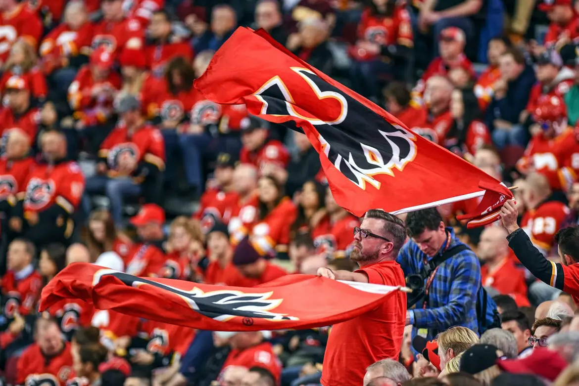 Fans enthusiastically wave red Calgary Flames flags at a packed hockey game.