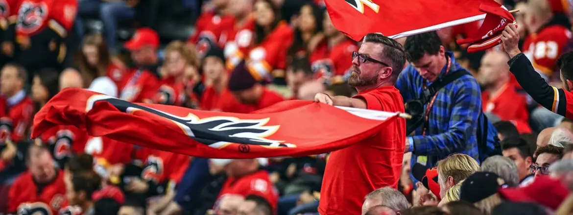 Man enthusiastically waves a large red flag at a crowded sports event.