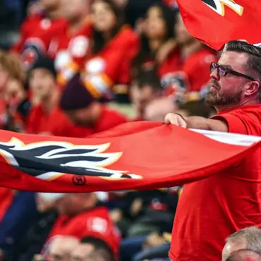 Man enthusiastically waves a large red flag at a crowded sports event.