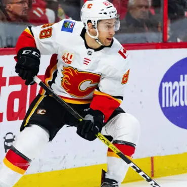 Hockey player in white Calgary Flames jersey skating on ice.