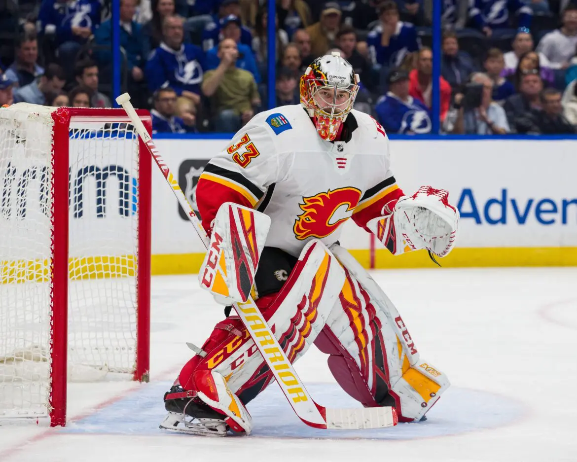 Goalie in white and red gear guards the net during a hockey game.