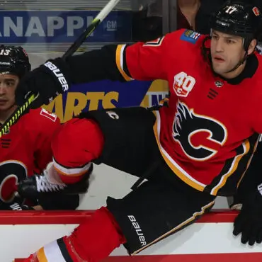 Two hockey players in red Calgary Flames jerseys in action on the ice.