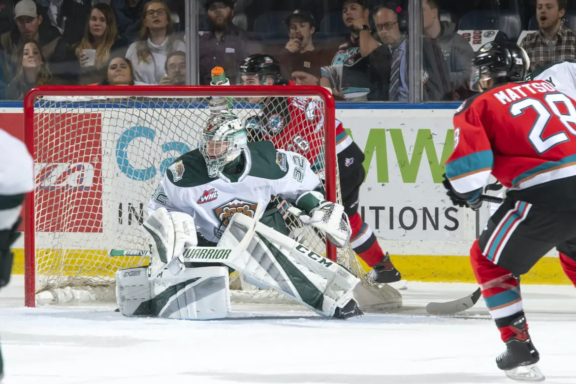 Hockey goalie in white pads blocking a shot during a game.
