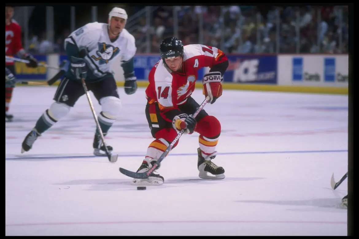 Hockey player in red and yellow uniform skating with the puck.