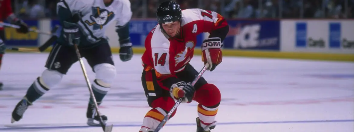 Hockey player in red and white uniform skating with puck on ice.