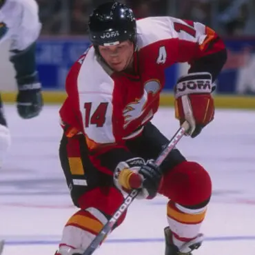Hockey player in red and white uniform skating with puck on ice.