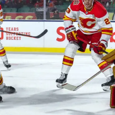 Two hockey players in red and yellow uniforms competing on ice.