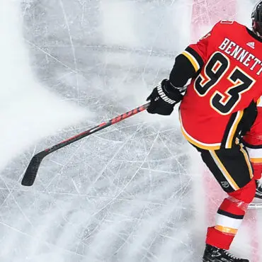 Hockey player in red and yellow jersey skating on ice with puck.