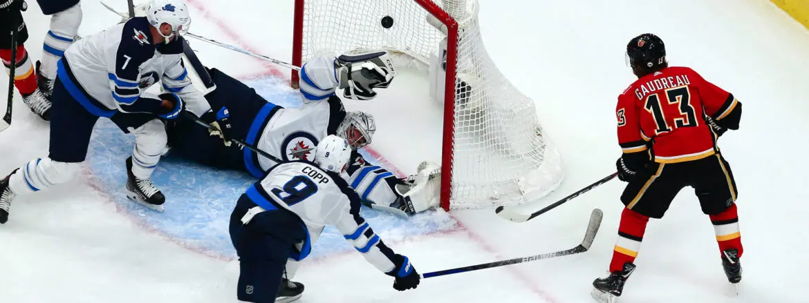 Hockey player attempts to score as goalie defends the net.