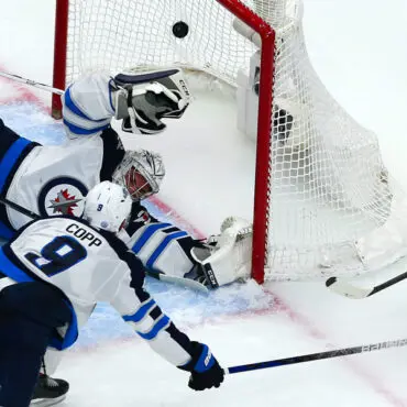 Hockey player attempts to score as goalie defends the net.
