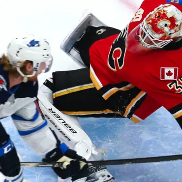Hockey goalie makes a diving save against a forward in white.