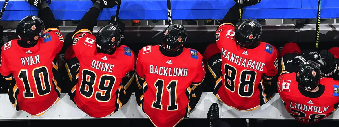 Three hockey players in red jerseys sitting on a bench, viewed from behind.
