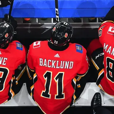 Three hockey players in red jerseys sitting on a bench, viewed from behind.