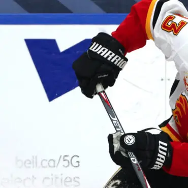 Hockey player in red and white gear controls the puck with a stick on ice.