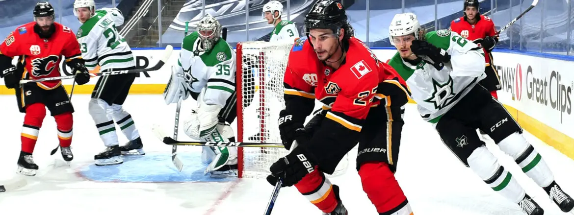 Hockey player in red and black jersey skating with puck near goal.