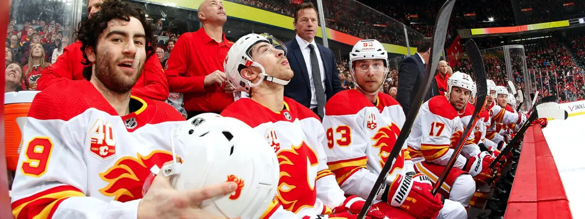 Two Calgary Flames hockey players sit on the bench during a game.