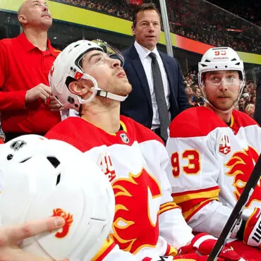 Two Calgary Flames hockey players sit on the bench during a game.