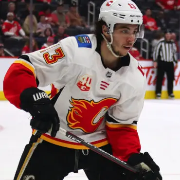 A hockey player in a white and red Calgary Flames jersey on ice.