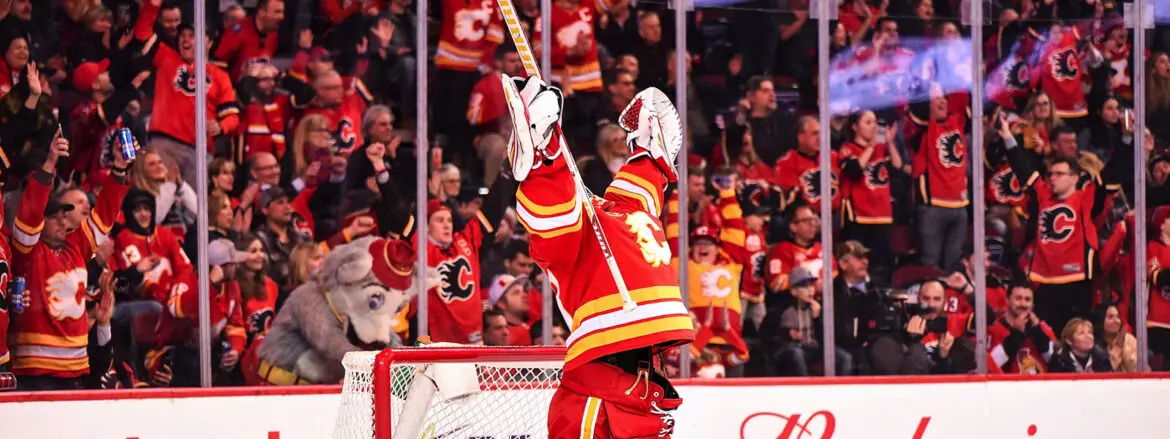 Hockey player celebrating a goal with raised arms in front of cheering fans.