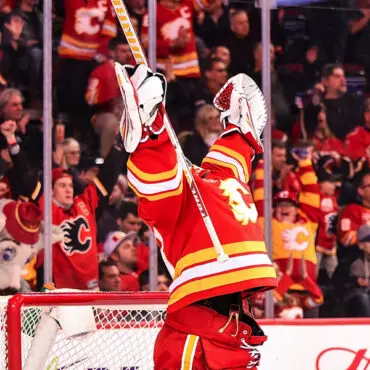 Hockey player celebrating a goal with raised arms in front of cheering fans.