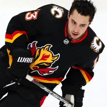 Hockey player in black Calgary Flames jersey skating intensely.