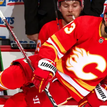 Two hockey players in red and orange jerseys competing for the puck.