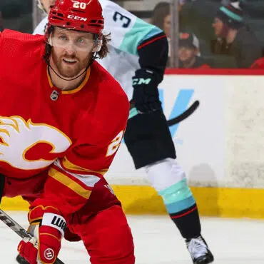 Hockey player in red Calgary Flames jersey skating on ice during a game.